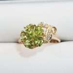 9ct gold ring featuring round peridot surrounded by 5 petal shaped peridot gems with leaf shaped design encrusted in diamonds